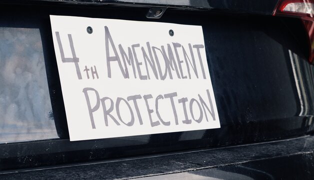 Man attaching protest license plates to vehicle using screwdriver, illustrating citizen pushback against ALPR surveillance - Fourth Amendment privacy