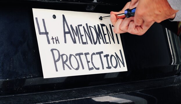 Man attaching protest license plates to vehicle using screwdriver, illustrating citizen pushback against ALPR surveillance - Fourth Amendment privacy