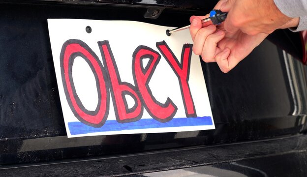Man attaching protest license plates to vehicle using screwdriver, illustrating citizen pushback against ALPR surveillance - Fourth Amendment privacy