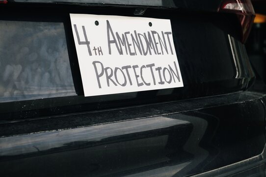 Man attaching protest license plates to vehicle using screwdriver, illustrating citizen pushback against ALPR surveillance - Fourth Amendment privacy