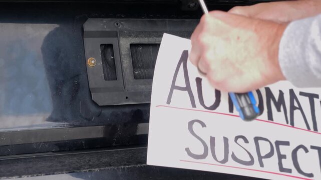 Man attaching protest license plates to vehicle using screwdriver, illustrating citizen pushback against ALPR surveillance - Fourth Amendment privacy