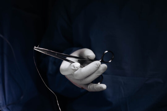 Close-up of gloved surgical hands holding a needle holder and suture thread during an operation, emphasizing precision, suturing technique and sterile surgical practice. Medical process and concept.