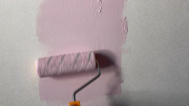 Woman's hand painting a textured wall with light pink paint using a roller. A home renovation, DIY repair, or interior decoration process.