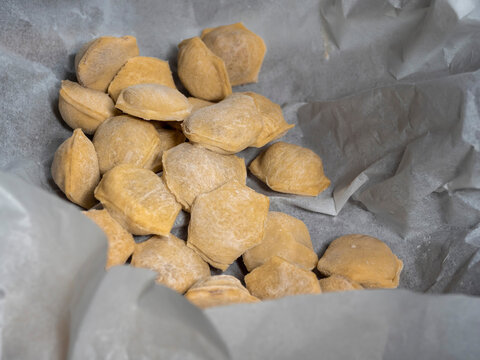 Freshly made, uncooked dumplings on parchment paper. Golden brown, irregularly shaped dumplings scattered across surface. Ready for cooking or baking, homemade style. Textured dough visible