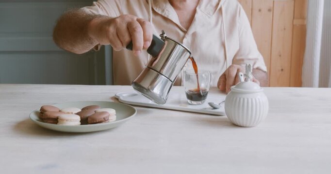Man making coffee at home with traditional Italian neapolitan moka pot and pouring into a glass coffee cup. Preparation home coffee, morning ritual, coffee brewing process.