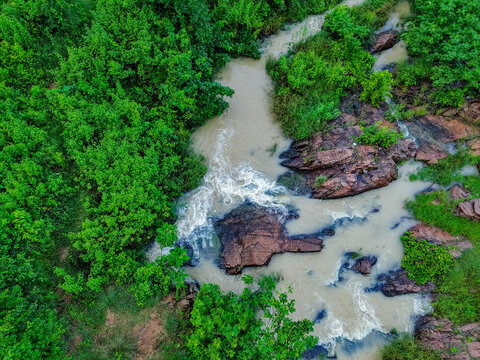 Aerial view of a stream flowing over rocky terrain surrounded by lush green vegetation in Mahilong, Jharkhand, India.