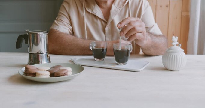 Man making coffee at home, putting cane sugar into glass coffee cup with hot coffee. Preparation home coffee, morning ritual, coffee brewing process.