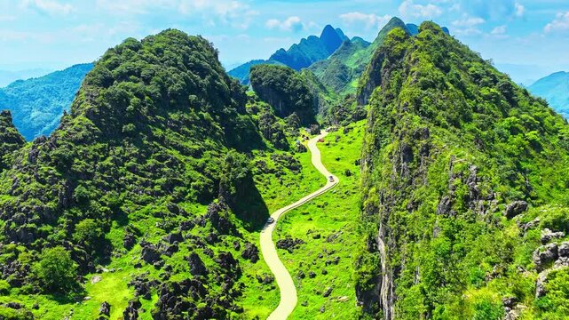 Winding mountain road through lush green peaks, rocky cliffs, and alpine meadow under a bright blue sky, ideal for travel and tourism campaigns.