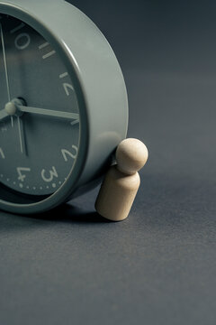 Wooden figurine crushed by the weight of time represented by an analog clock