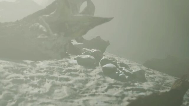 A foggy area shows broken pieces of wood and rocks on a sandy surface. Large rocks are barely visible through the fog, creating an unknown atmosphere.