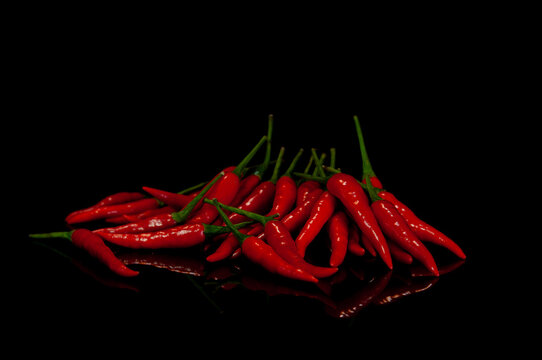 Fresh red chili peppers on a glossy black reflective surface with copy space. Dramatic food still life featuring vibrant spicy ingredients.