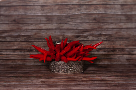 Red chili peppers in an embossed metal bowl on a wooden background. Fresh spicy ingredients in a rustic farmhouse still life.