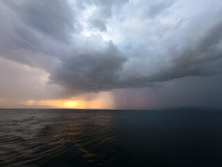 Fototapeta premium Dramatic Thunderstorm Over the Sea with Rain Curtain and Glowing Sunset Horizon