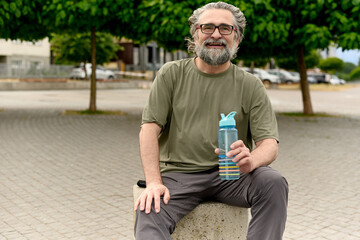Fototapeta premium Smiling senior man resting with water bottle after workout