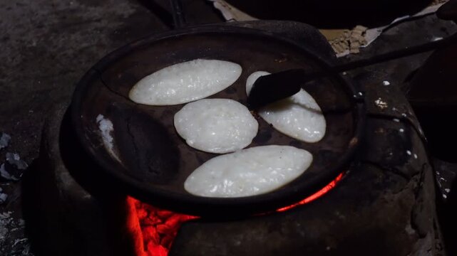 A woman brings out the finished Chitai Pitha in a hot clay oven. Chitai pitha is being made in a terracotta mold for making pitha in a heated clay oven.