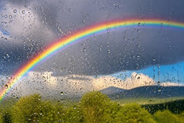 Obraz premium Rainbow arching over wet window and green landscape