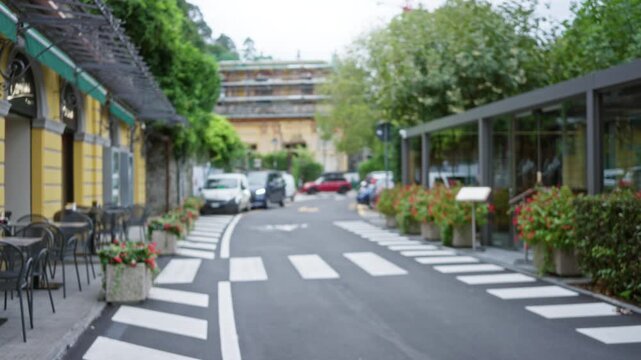 Defocused street background with soft bokeh, cafe terraces, crosswalk and planters along an outdoor city lane; background backplate copyspace template.