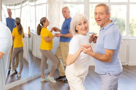 Group of happy elderly pensioners learning to dance latin dances in dance studio