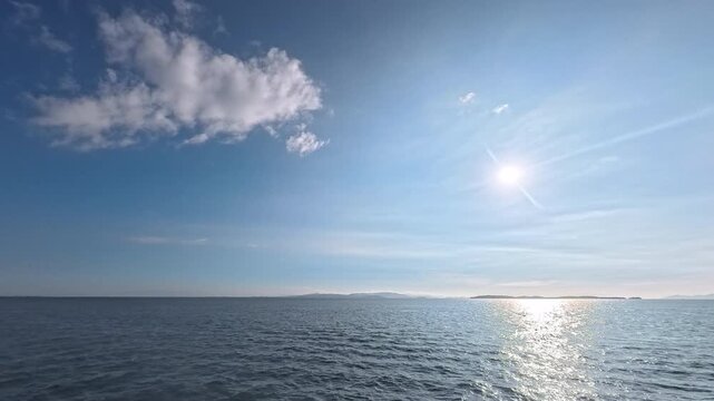 Cinematic real-time video of fluffy white cloud and bright sun over ocean horizon for weather forecast and backdrop