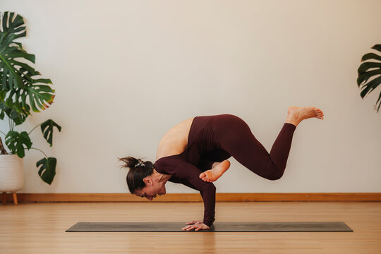 Photographic woman holds a yoga balance pose on a mat in a studio with tropical plants, promoting wellness and strength
