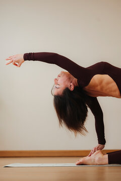 Woman performs a graceful yoga balance pose in a warm studio, natural photography on a beige background, conveying wellness