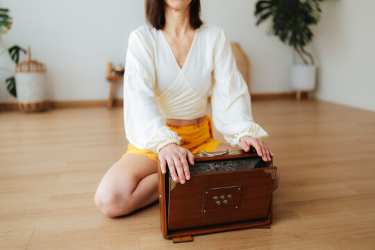 Woman seated with a harmonium in a bright home, soft photographic style, wooden floor background, mindfulness and music concept