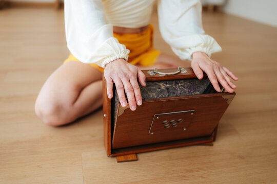 Close-up photograph of a woman playing a wooden harmonium, soft focus, warm indoor floor background, music, tradition and devotion