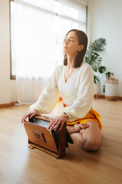 Woman meditates cross-legged with harmonium in a bright home, soft photographic style, peaceful wellness concept, warm light