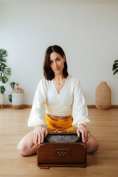 Woman sits cross-legged with a harmonium in a bright room, photographic style, on a neutral background, wellness concept