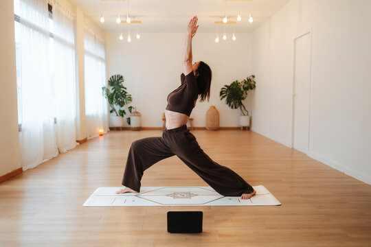Woman holding a yoga warrior pose on a mat in a bright studio, warm photographic style, indoor background, wellness concept