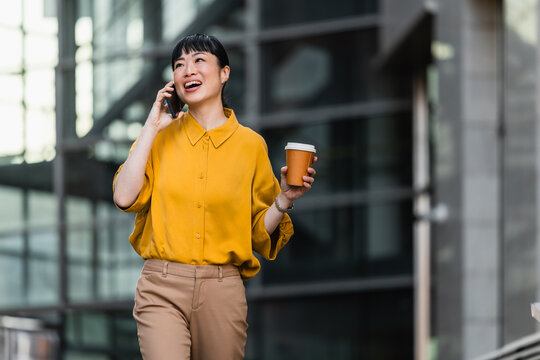 Young professional woman walking in city, talking on phone and holding takeaway coffee