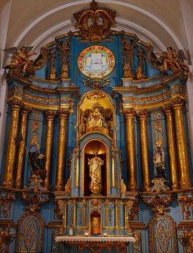 Ornate Baroque church altarpiece with gilded columns, blue wooden retablo, religious statues and stained glass window in a historic colonial church interior