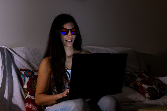 Woman wearing blue light blocking glasses while working on laptop at night
