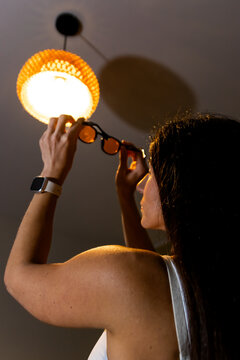 Woman holding orange protective goggles blocking light from ceiling lamp