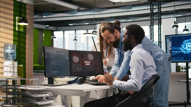 Programmer requests help from coworkers after a critical error warning appears, and the office team brainstorms how to fix a computer bug affecting software systems and applications.
