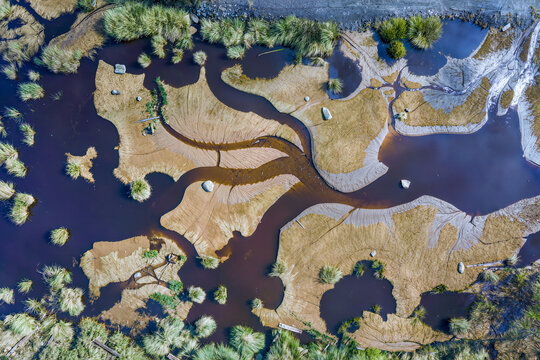 Top down aerial view of braided river channels cutting between sculpted sandbars, boulders and tussock grass