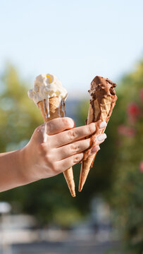Hand holding melting vanilla and chocolate ice cream cones against blue summer sky. Sweet dessert, hot weather, refreshing food with copy space.