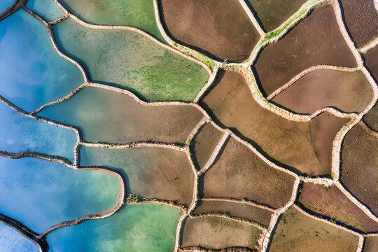 Top down aerial view of irregular flooded ponds shading from bright blue and green into bare brown mud flats