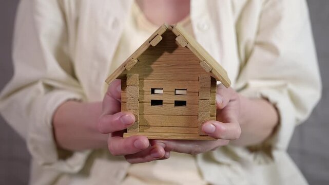 Losing a home. Woman's hands are carefully holding a small wooden house model, which then falls apart and is crushed, symbolizing concepts of destruction, loss of home, foreclosure, financial crisis