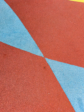 Brightly colored playground surface shows red and blue sections meeting at an angle during daytime