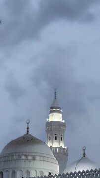Illuminated minaret and white domes of Masjid Al Qiblatain in Medina at twilight.