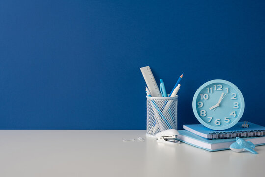 Side view photo of back to school stationery and blue alarm clock on desk