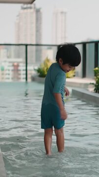 Happy young boy splashing in a rooftop pool with a city view