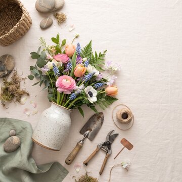 A charming still life composition showcasing a vibrant bouquet of spring flowers in a rustic ceramic vase, surrounded by gardening tools and natural elements.