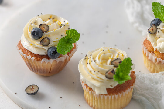 Delicious vanilla cupcakes with white frosting fresh blueberries mint and chia seeds on a marble board