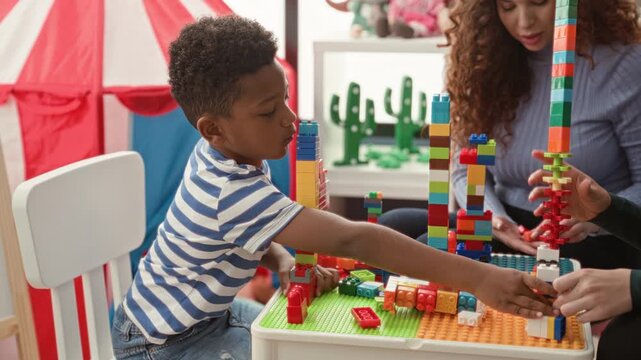 Boy stacking tall colorful block tower with adult hand steadying and his reaching hand in building; concentration teamwork.