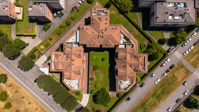 Architectural Geometry: An aerial view reveals a symmetrical building with a terracotta-tiled roof, surrounded by manicured greenery and a paved road, showcasing precise urban design and structure.