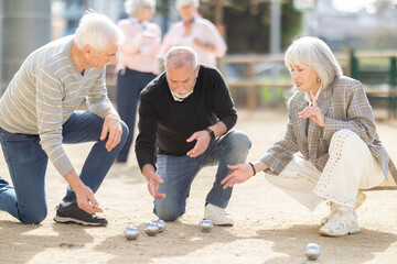 Fototapeta premium Attentive retired seniors discussing the competition while enjoying petanca on a sunny day