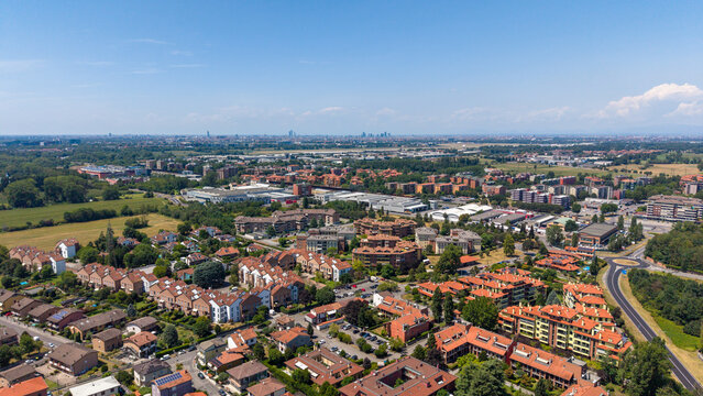 Suburban Panorama: A sprawling view of a modern suburban town under a clear blue sky, showcasing residential houses, apartment buildings, and lush green spaces. Bellaria, Peschiera Borromeo, Italy