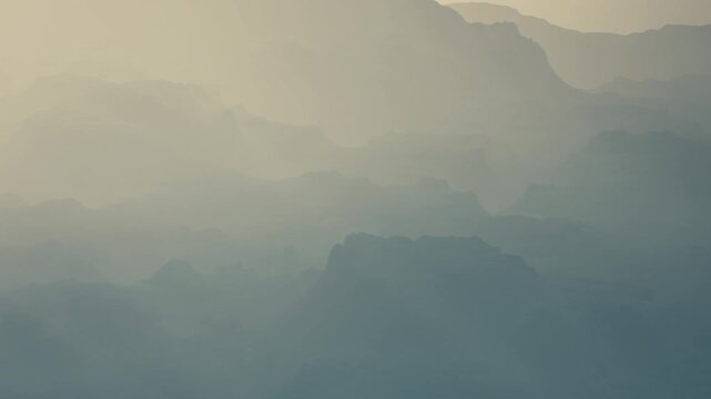Fog covers the mountains in a valley during the early morning. The light creates a soft atmosphere, making the landscape appear gentle. There are layers of mountain and mist.